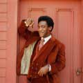 Decked out head to toe in a brown corduroy suit while holding a cigar and leaning against a door, Bill Cosby can be seen with his trademark pursed lips and smirk. This classic image of Cosby was taken by Milton H Greene in Hollywood in 1969.