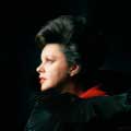 Photograph of Judy Garland in a stunning portrait by Milton H. Greene showing Judy in a black ruffled dress looking off in the distance behind a dark black background.