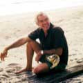 While on a photographic assignment for McCalls in 1969, Milton H Greene took this color image of action star Lee Marvin sitting on a beach. Lee is seated and wearing shorts looking off to the left while holding a large sport-style fishing reel.