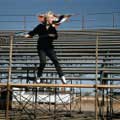 Marilyn Monroe stands in empty rodeo grandstands while holding a rail in the on location image from her movie Bus Stop. Taken in 1956 by Milton H. Greene, Marilyn black and white striped pants while looking off to the right.