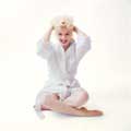 Sexy photograph showing Marilyn Monroe gritting her teeth and smiling widely, grabbing her hair with both hands and sitting cross legged wearing only a white robe against a white background. Milton H Greene took this image in his New York Studio in 1955.