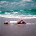This classic fashion photograph was taken in 1954 by Milton H. Greene while on assignment for look Magazine. Wearing vintage white one-piece bathing suit, model Carmen is laying on the Manalapan Beach, Florida sand getting some sun while the ocean waves crash just behind her.