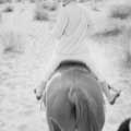 Candid black and white photograph of Marilyn Monroe wearing white courdoroy suite and black head band looking back on horse back in California by Milton H. Greene in 1954. 