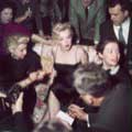 Milton H Green took this classic photo of a stunning Marilyn Monroe wearing a black spaghetti dress while speaking to reporters during a cocktail party in 1956. The reporters have surrounded Marilyn as she calmly answers a question while sitting on a couch in Greene's home.