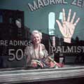 In an image from the popular The Gypsy Sitting, Marilyn Monroe is smiling widely behind the window of a gypsy palm reader shop on the 20th Century Fox back lot. Milton H Greene took this photo in 1956.