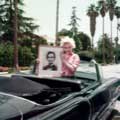 Wearing a red checkered shirt, Marilyn Monroe is smiling while holding a framed photo of her idol, Abraham Lincoln. Taken by Milton H Greene in Los Angeles 1954, Marilyn is standing in her brand new black Cadillac given to her by Jack Benny. Palm trees can be seen in the background.