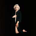 In this iconic color image by Milton H Greene, Marilyn Monroe is nude except for a black sweater. Kneeling against a black background, Marilyn is looking directly at the camera and using her right hand to hold her sweater closed near her breasts and her left hand is down by her legs. Milton took this risqué photo for Look magazine in 1953 during their First Sitting and it appeared on the cover of Playboy January 1997.