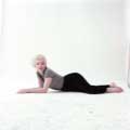 Laying on the ground wearing black pants and a gray and black striped top, Marilyn Monroe is seductively looking at the camera against a white backdrop. Taken by Milton H Greene in his New York Studio in 1956.