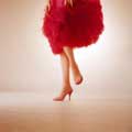 Color vintage fashion photograph of a model's legs wearing a red feather dress and red high heels. her left leg is slightly raised and her hands with red nail polish are just seen at the top of the classic image by Milton H Greene on assignment for Life magazine in 1958.