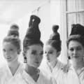 Legendary Fashion photographer Milton H. Greene snapped this classic black and white vintage fashion image in Paris 1962. Four models have their hair up in unique, tall buns and are wearing white collared shirts. Two of the models are smiling and looking at the camera. 